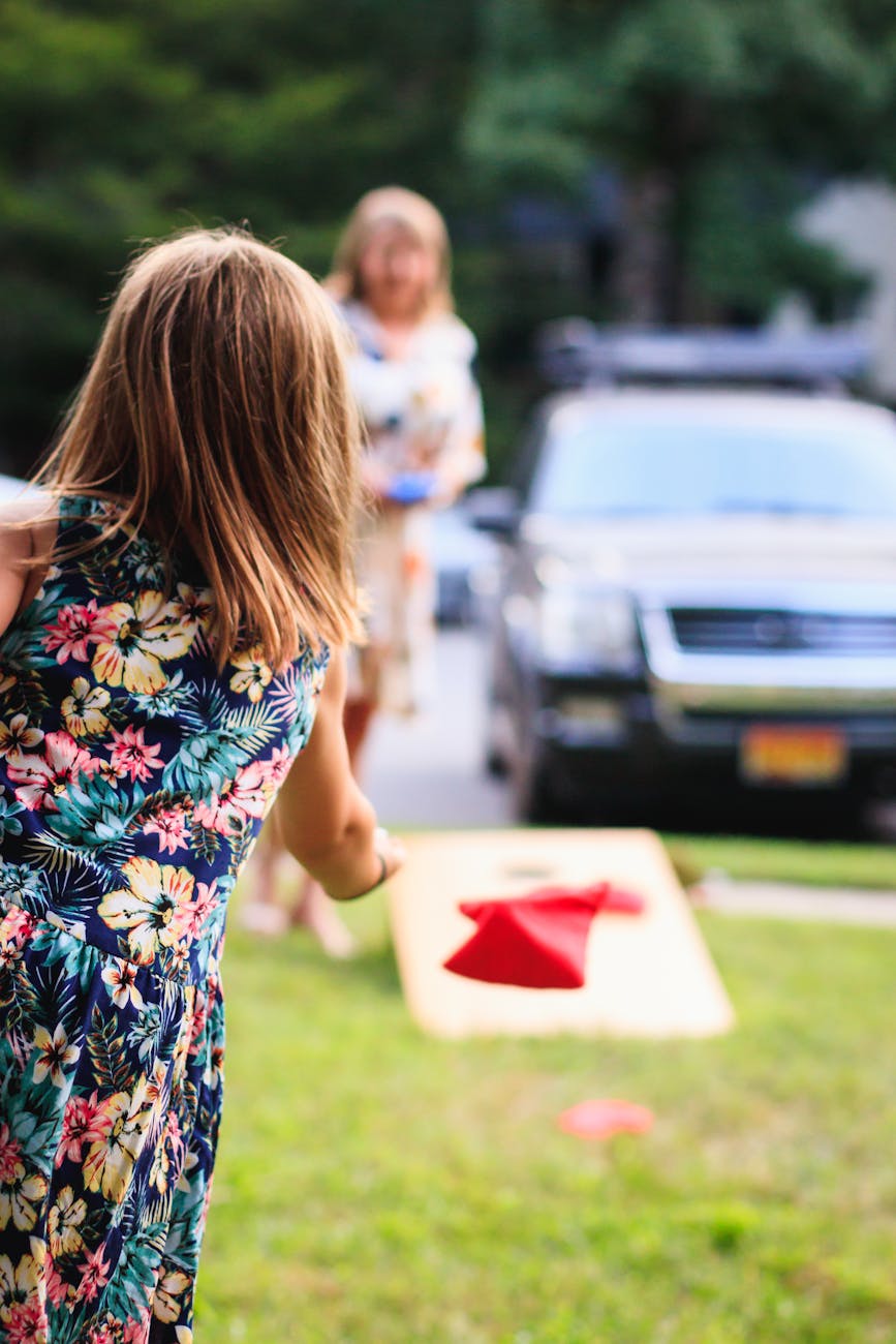 girl wearing multicolored floral sleeveless dress throwing red handkerchief standing on green grass during daytie